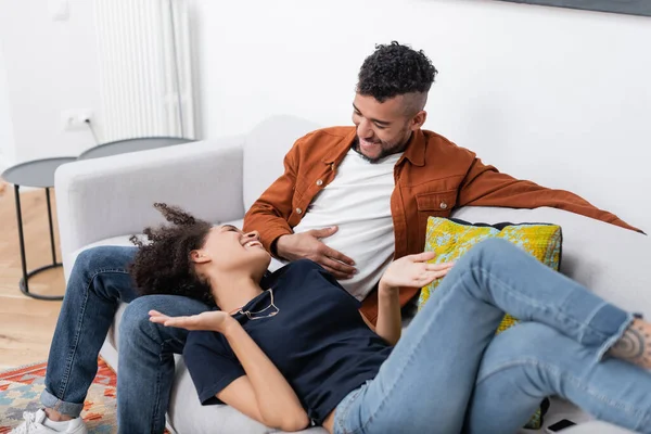 Heureux couple afro-américain se regardant tout en se reposant sur le canapé dans un appartement moderne — Photo de stock