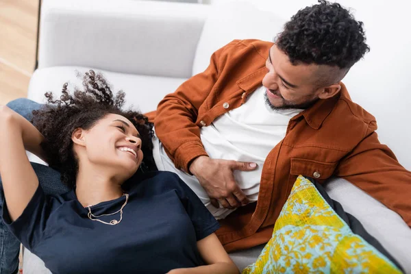 Hochwinkelaufnahme eines fröhlichen afrikanisch-amerikanischen Paares, das sich beim Liegen auf der Couch anschaut — Stockfoto