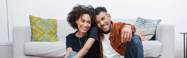 Mujer americana africana alegre y novio feliz sonriendo en apartamento moderno, bandera - foto de stock