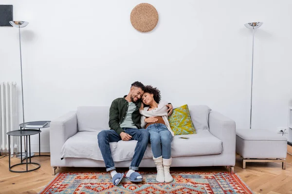 Femme enceinte afro-américaine assis avec mari heureux sur le canapé dans un appartement moderne — Photo de stock