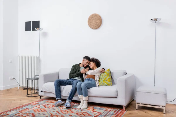 Femme enceinte afro-américaine assis avec mari heureux sur le canapé dans un appartement moderne — Photo de stock