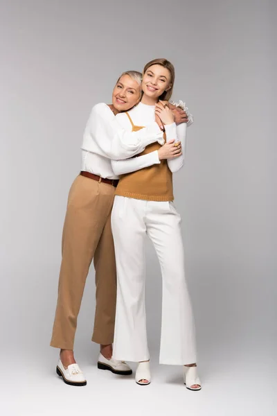 Full length of happy middle aged mother hugging young daughter on grey — Stock Photo