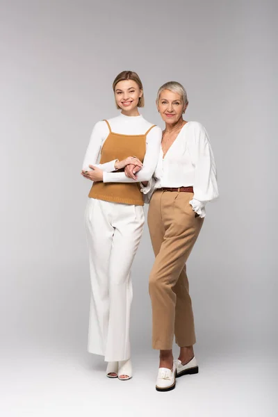 Full length of happy middle aged mother standing with hand in pocket near young daughter on grey — Stock Photo