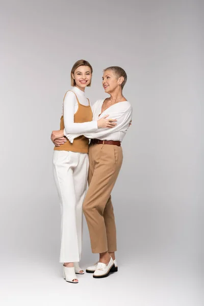 Full length of pleased middle aged mother and young daughter hugging on grey — Stock Photo