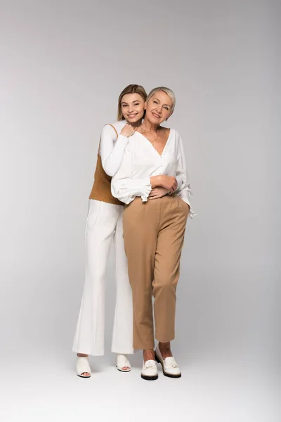 Full length of pleased young daughter hugging middle aged mother on grey — Stock Photo