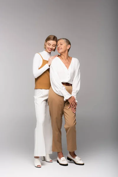 Full length of pleased young daughter standing with happy middle aged mother on grey — Stock Photo