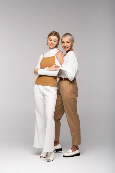 Full length of pleased middle aged mother standing with happy young daughter on grey — Stock Photo