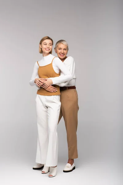 Full length of pleased middle aged mother hugging happy daughter on grey — Stock Photo