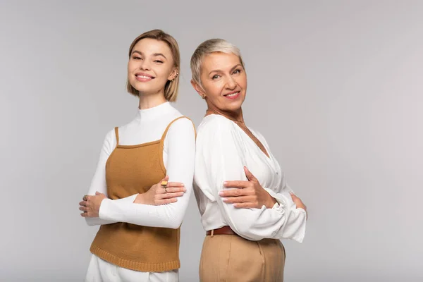 Glückliche Mutter mittleren Alters und freudige kleine Tochter stehen mit verschränkten Armen isoliert auf grau — Stockfoto