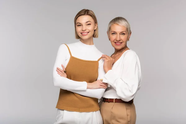 Heureuse mère d'âge moyen près de la jeune fille debout avec les bras croisés isolés sur gris — Photo de stock