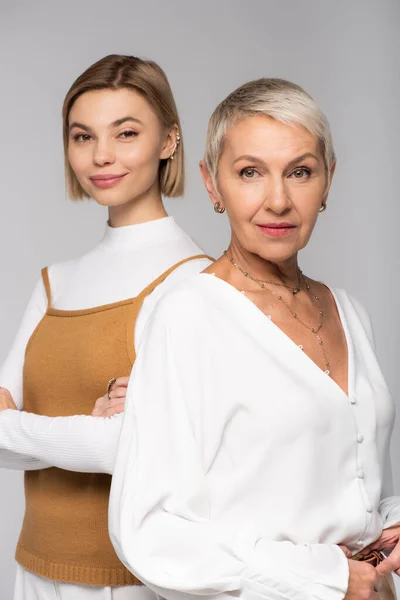 Mutter mittleren Alters in der Nähe einer glücklichen kleinen Tochter mit verschränkten Armen isoliert auf grau — Stockfoto