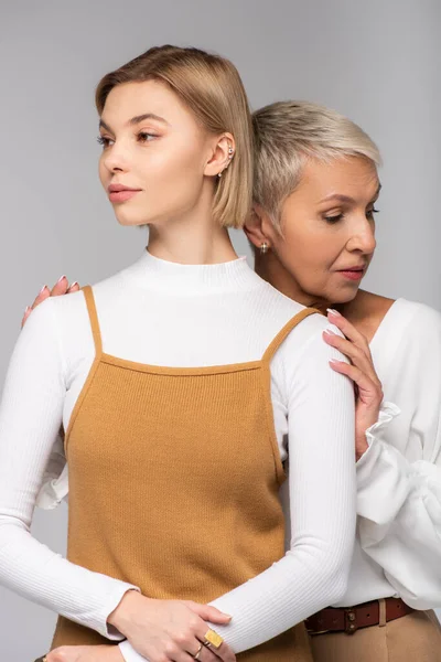 Madre de mediana edad abrazando hija joven mirando hacia otro lado aislado en gris - foto de stock