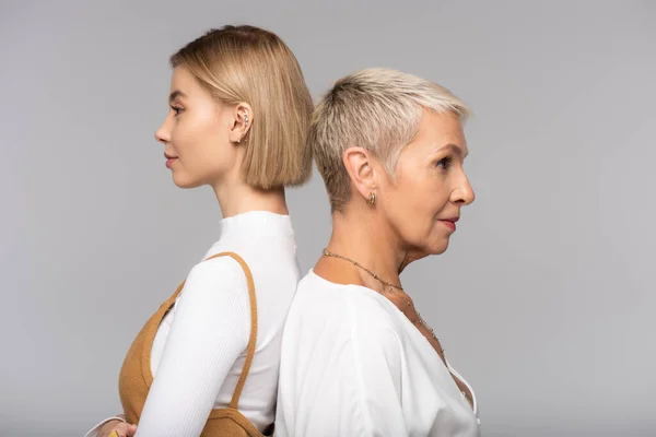 Seitenansicht junge Frau steht Rücken an Rücken Mutter mittleren Alters isoliert auf grau — Stockfoto
