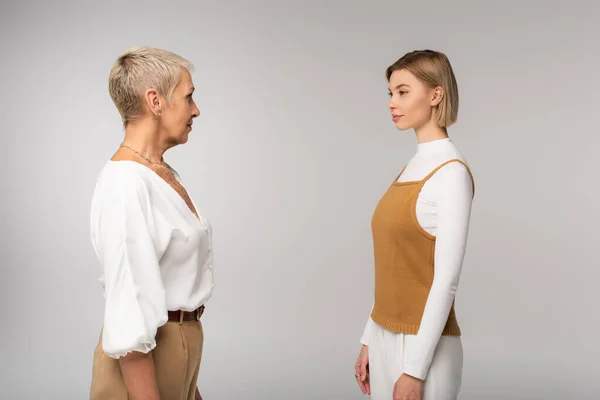 Young daughter and mature mother looking at each other isolated on grey — Stock Photo