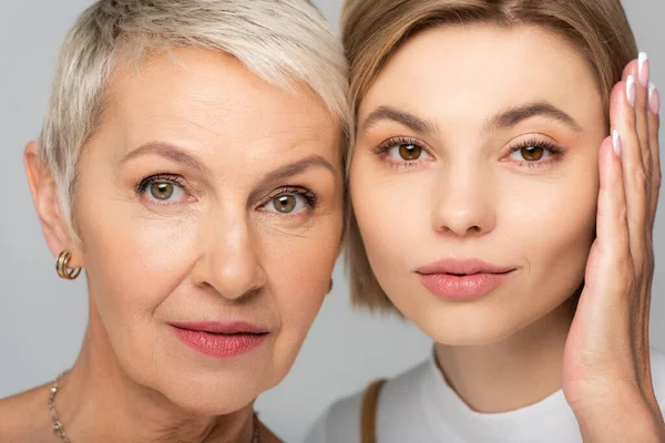 Close up of pretty young woman and mature mother looking at camera isolated on grey — Stock Photo