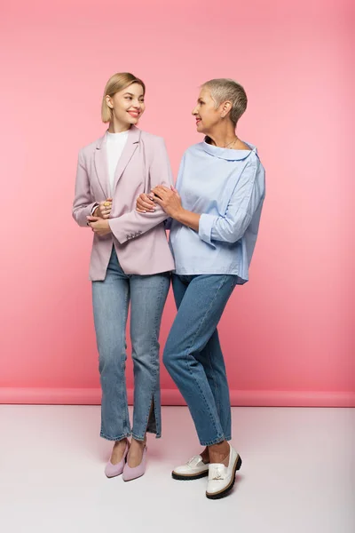 Comprimento total da jovem mulher feliz e maduro mãe em jeans e blusa de pé em rosa — Stock Photo