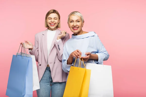 Jovem mulher alegre e mãe madura feliz segurando sacos de compras isolados em rosa — Fotografia de Stock