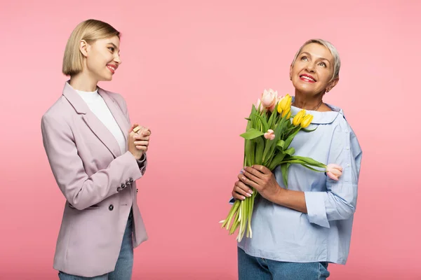 Mãe de meia idade feliz segurando buquê de flores perto da filha satisfeita isolada no rosa — Fotografia de Stock