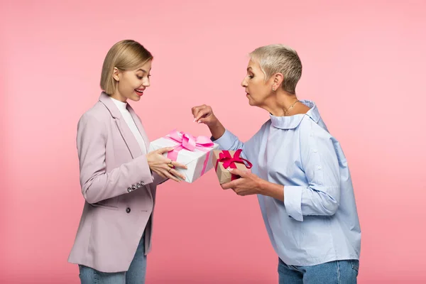 Усміхнена молода дочка і зріла мати тримає подарунки ізольовані на рожевому — стокове фото