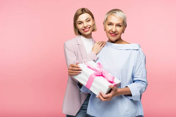 Glücklich reife Mutter hält Geschenk nahe Tochter isoliert auf rosa — Stockfoto