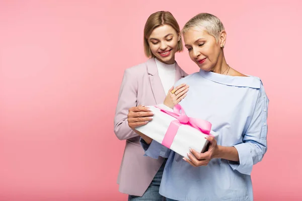 Щаслива зріла мати тримає подарунок біля задоволеної молодої дочки ізольовано на рожевому — стокове фото