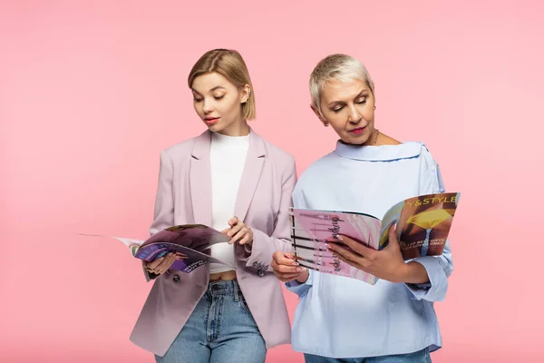 Mature mother and young daughter reading magazines isolated on pink — Stock Photo