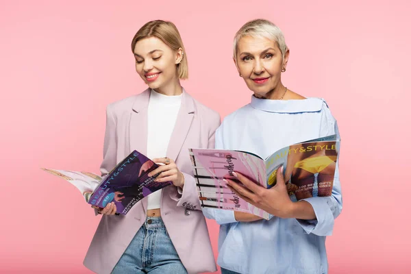 Reife Mutter und glückliche junge Tochter lesen Zeitschriften isoliert auf rosa — Stockfoto