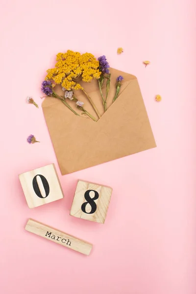 Vue de dessus des fleurs sèches dans une enveloppe artisanale avec des fleurs sèches près de cubes en bois avec 8 mars sur rose — Photo de stock
