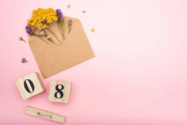 Top view of dry flowers in craft envelope with dried flowers near wooden calendar cubes with 8 march on pink — Stock Photo