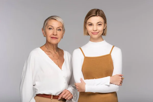 Feliz mujer de mediana edad de pie cerca de sonriente hija joven aislado en gris - foto de stock