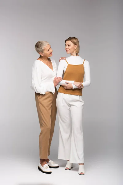 Full length of middle aged woman looking at young happy daughter on gray — Stock Photo