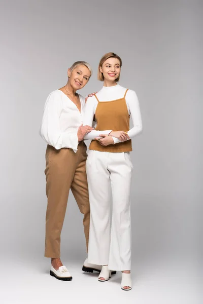 Full length of happy middle aged woman standing near smiling young daughter on gray — Stock Photo