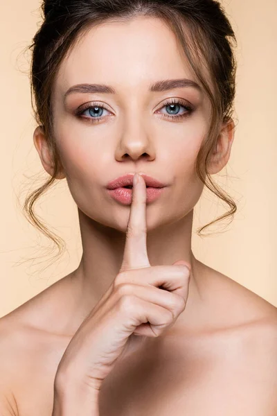 Giovane donna mostrando gesto segreto a macchina fotografica isolata su beige — Foto stock