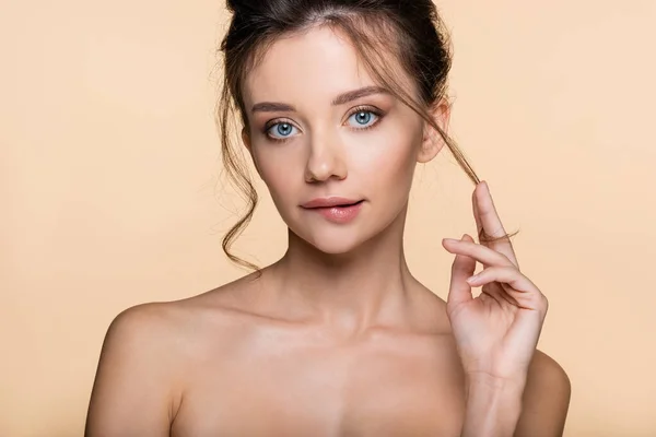 Bonito modelo tocando el cabello y mordiendo el labio aislado en beige - foto de stock