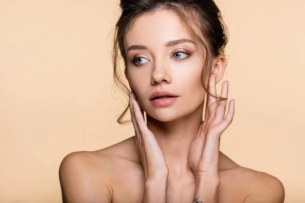 Pretty model with naked shoulders touching face isolated on beige — Stock Photo