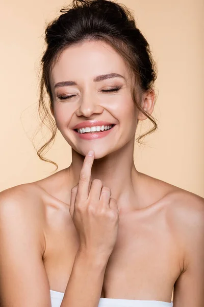 Happy brunette woman touching chin isolated on beige — Stock Photo