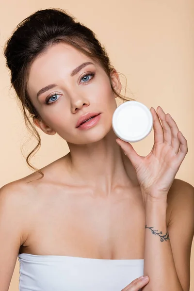Junge Frau in weißem Top-Aufbewahrungsbehälter mit Kosmetikcreme isoliert auf beige — Stockfoto