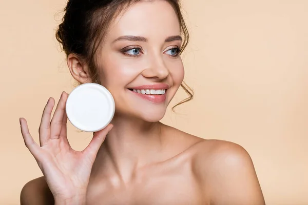 Positive model with naked shoulders holding cosmetic cream isolated on beige — Stock Photo