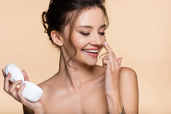 Positive model with naked shoulders applying cosmetic cream on nose isolated on beige — Stock Photo