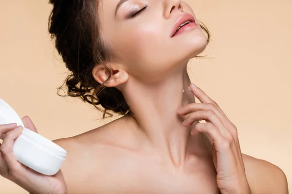 Обрезанный вид молодой женщины, наносящей косметический крем на шею, изолированный от бежевого цвета — стоковое фото