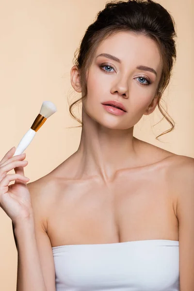 Model in white top holding cosmetic brush isolated on beige — Stock Photo