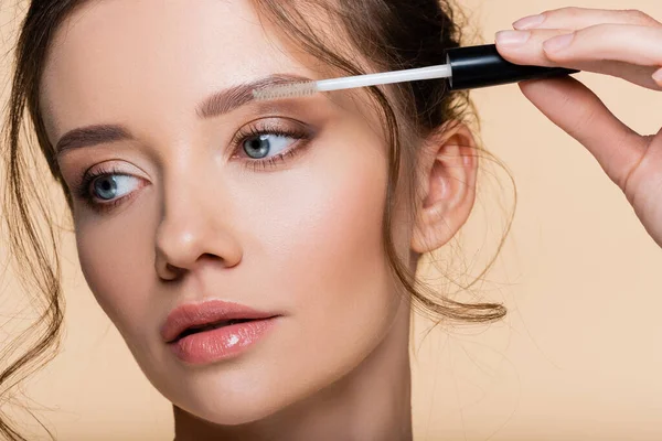 Portrait of woman holding brush of eyebrow gel isolated on beige — Stock Photo