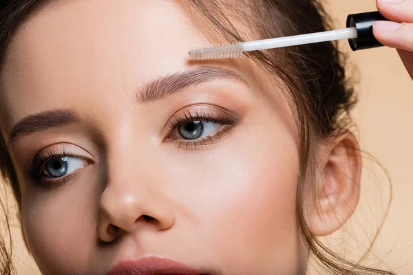 Vue recadrée d'une jeune femme appliquant un gel pour sourcils isolé sur beige — Photo de stock