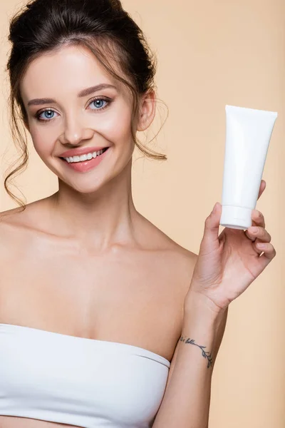 Cheerful model holding tube with lotion isolated on beige — Stock Photo