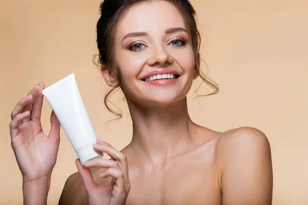 Brunette woman with naked shoulders holding cosmetic lotion isolated on beige — Stock Photo