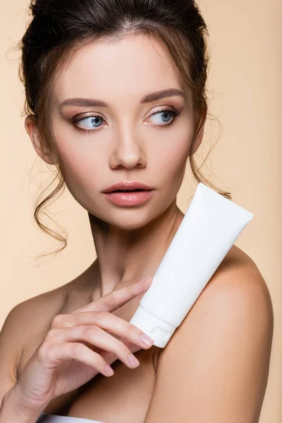Jeune modèle tenant lotion cosmétique près de l'épaule nue isolé sur beige — Photo de stock
