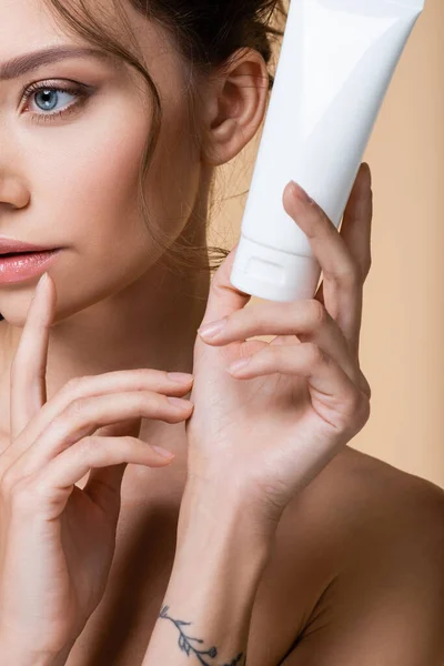 Cropped view of young model holding tube with lotion isolated on beige — Stock Photo