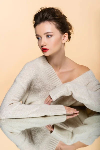 Brunette woman in sweater with naked shoulder looking away near mirror isolated on beige — Stock Photo