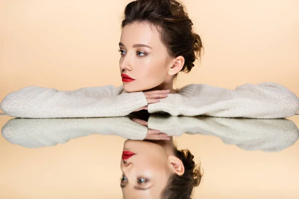 Giovane donna con labbra rosse in posa e guardando lontano vicino specchio isolato su beige — Foto stock