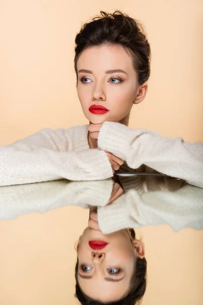 Hübsches Model in kuscheligem Pullover schaut in der Nähe von Spiegel isoliert auf Beige weg — Stockfoto